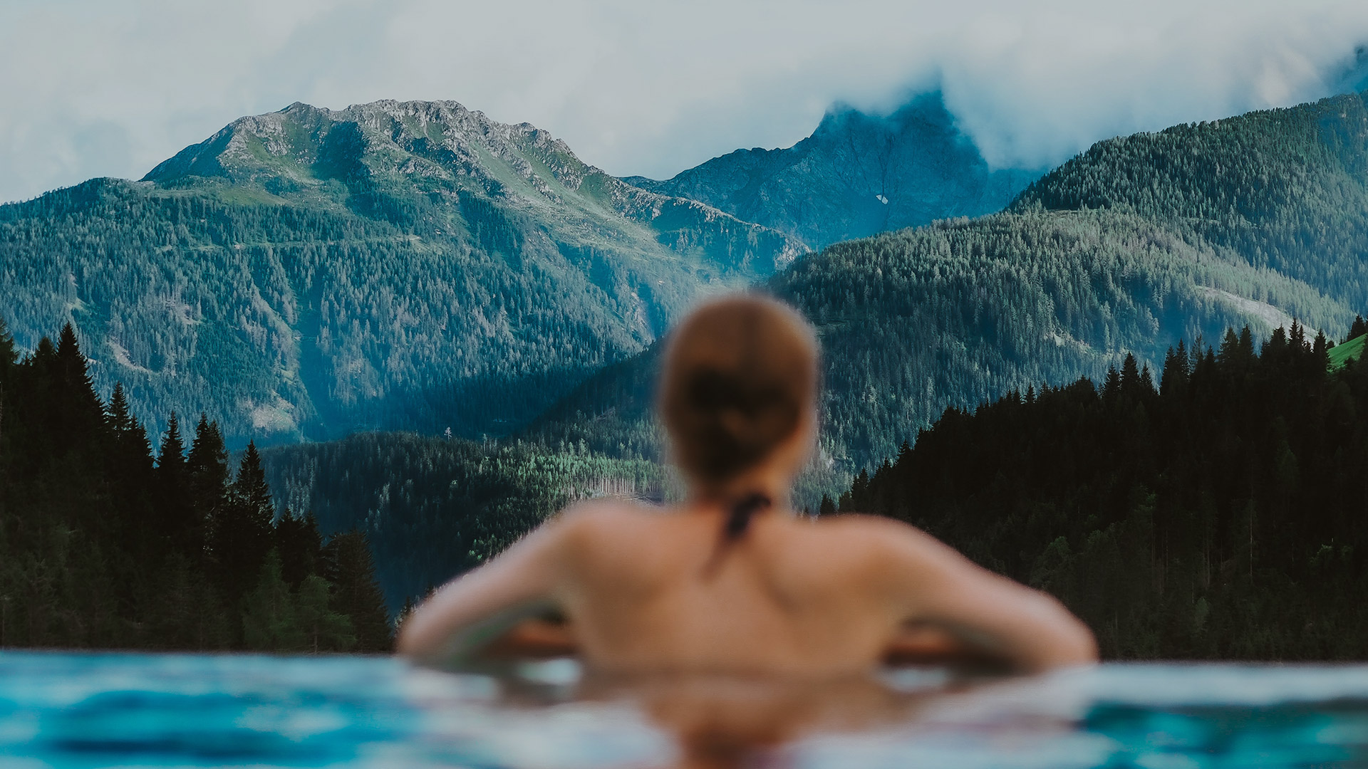 Eine Frau entspant sich in einem Badefass mit einem Blick auf Bergen.